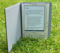 Our editors explain the pros and cans associated with e-book publishing. A photograph of a Sony eBook Reader resting in the grass. This shows the overall versatility of e-books and the value of e-book publishing.