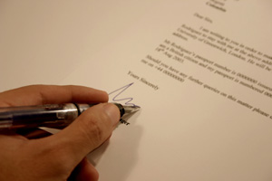 Our editors explain how to write a query letter. A close-up of a hand signing a query letter with a ballpoint pen.