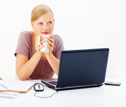 A woman is sitting in front of her computer. She is holding a cup of coffee, staring off into space, and debating about whether she should participate in NaNoWriMo.