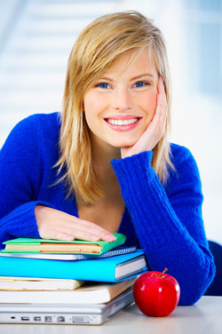 Our editors break down how to write an APA paper. An attractive young woman wearing a bright blue sweater sits behind, and rests her hands on, a stack of books containing information on APA style formatting.