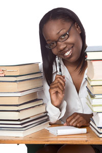 Our editors review free citation software. A young female student with a pen and notepad is sitting by a pile of books; she is debating about using online citation software to help write her bibliography.