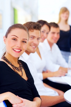 Our editors provide a sample of a cirriculum vitae. Five people are sitting on the same side of a table. The focus is on the first women, she is smiling and wearing a black dress.