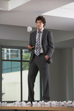 Scribendi.com's guide to beating writer's block. A man in a business suit is standing on a table covered in crumpled papers; he has conquered his writer's block.