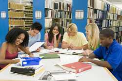Our editors provide a book review example. Six students are sitting around a table reading books and studying. They have a book review example on the table.