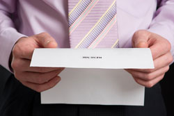 Our editors provide a sample candidate rejection letter. A man is holding an example candidate rejection letter. He is wearing a purple shirt and purple tie and only his midsection is visible in the photo.