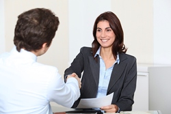 A women and a man are sitting at a table. His back is to the camara and they are shaking hands.