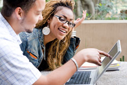 A male student points to a persuasive essay on his laptop; he is trying to persuade a female student to see his argument.