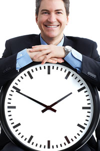 Business man standing with a large clock illustrating time management techniques.