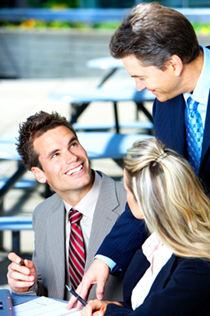 Three office employees are discussing a document at a conference table.