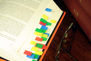 A large Turabian style reference book is open on a table. There are a number of multi-colored page markers stuck throughout. A pair of glasses is resting beside the book.
