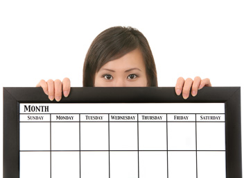 Our editors explain how to use an editorial calendar and why it is important. A woman is holding a large editorial calendar. The calendar covers the bottom half of her face and most of her body.