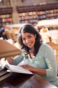 A young woman sitting in the library with Turabian Bibliography books. 