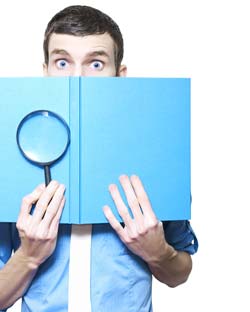 A book reviewer holds a blue book and magnifying glass.