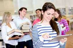 A woman standing with an e-reader in front of four people holding books. The four people holding books are wondering how to make an e-book.