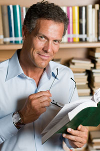 A male publisher is holding a book in his office library.