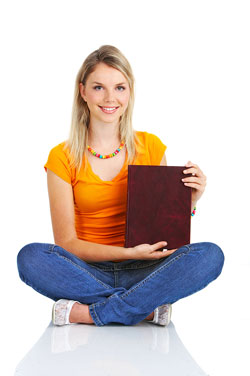 A young woman with blonde hair is sitting crossed-leg on the floor holding the book that she just self-published.