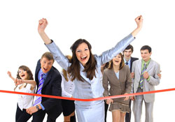 Scribendi.com holds a short story contest with a grand prize of up to $5,000. A woman in a business suit is crossing the finish line because she just won a short story contest. There are seven people in business attire close behind her.